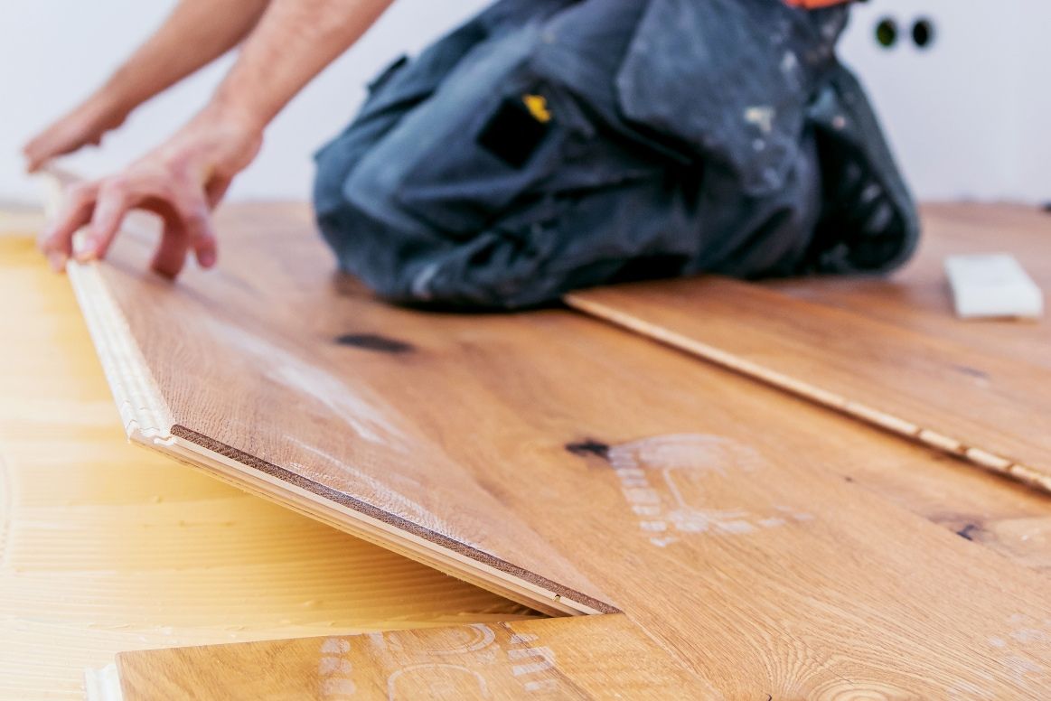 man wearing blue jeans installing wood floor panel.